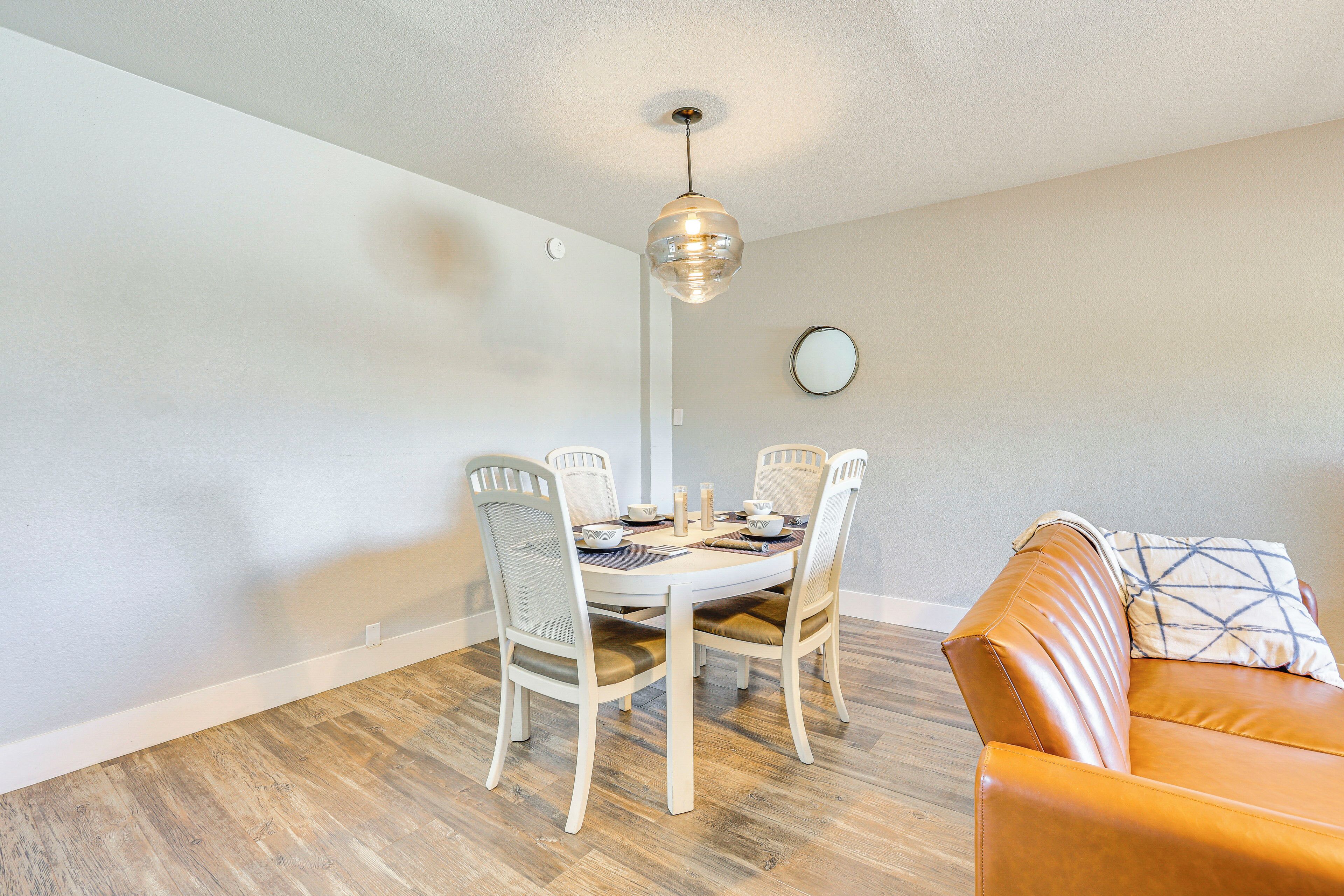 Un coin repas avec une table et des chaises blanches, un luminaire suspendu et un canapé en cuir marron.