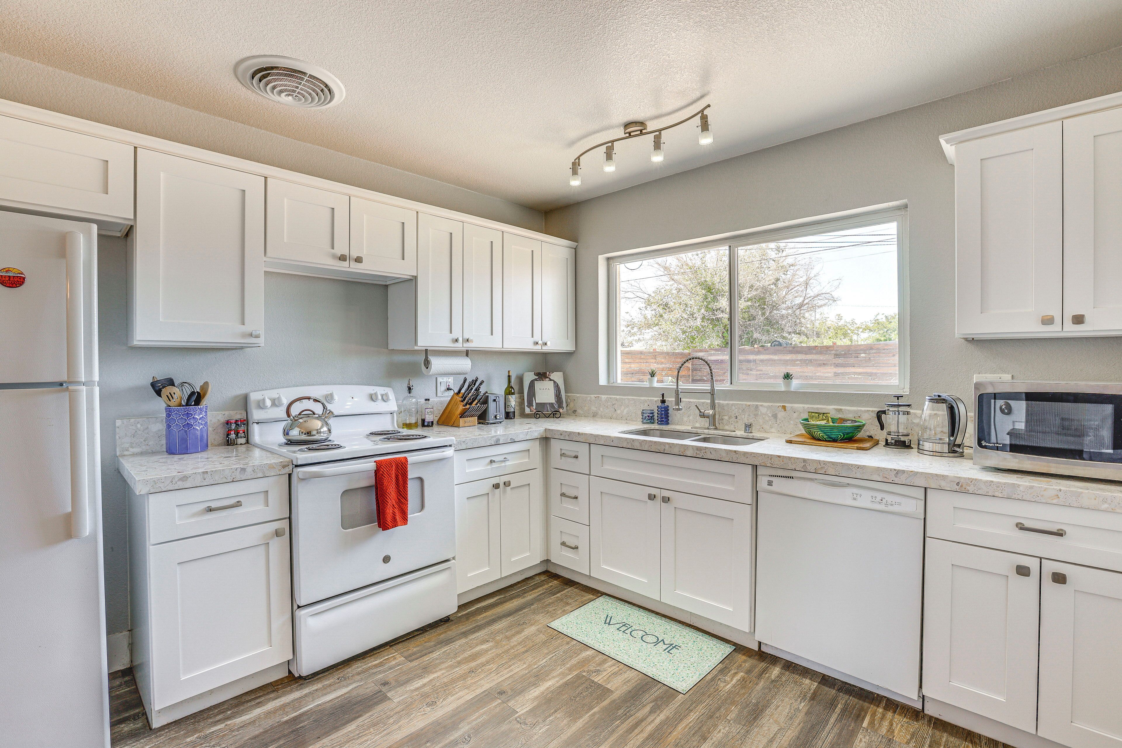 A kitchen with white cabinets, a stove, a sink, and a microwave.
