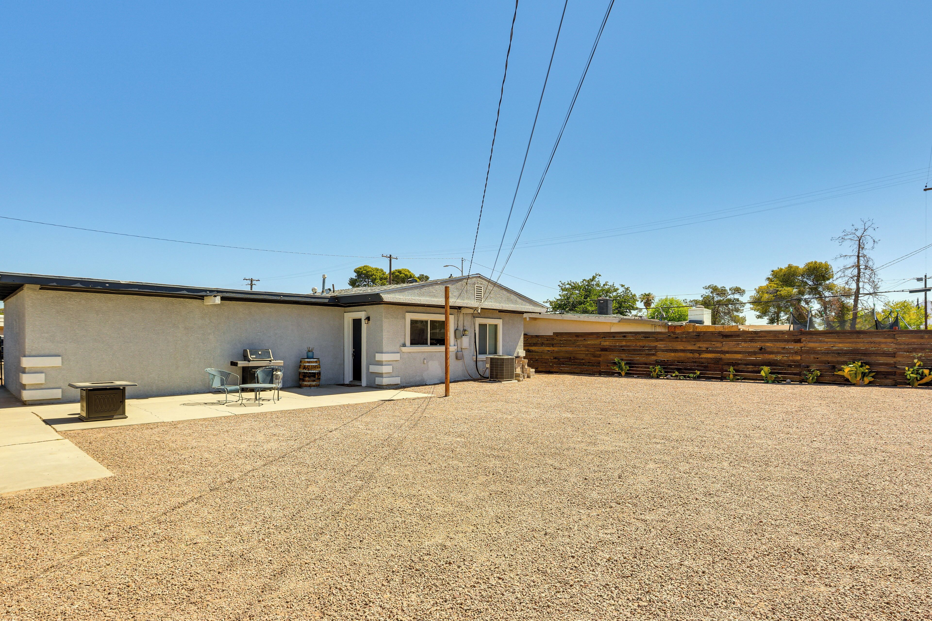 A modern house with a gravel driveway, a small patio with a table and chairs, and a wooden fence in the background.