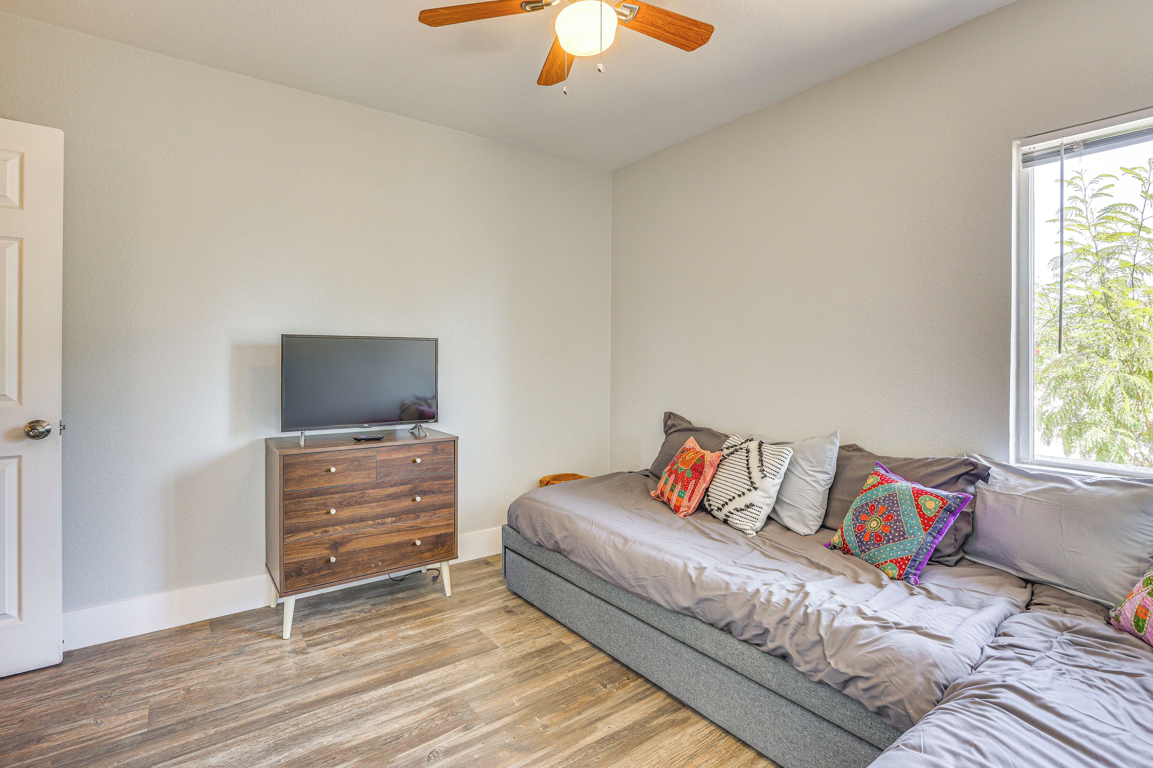 A bedroom with a bed, a dresser, a television, and a window with a view of trees.