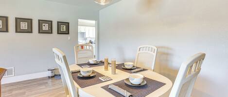 A dining area with a round table, white chairs, and a hanging light fixture.