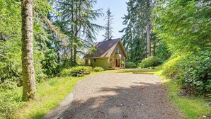 A rustic cabin surrounded by dense forest, accessible via a gravel path.