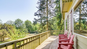 A wooden deck with red Adirondack chairs, overlooking a forested area.