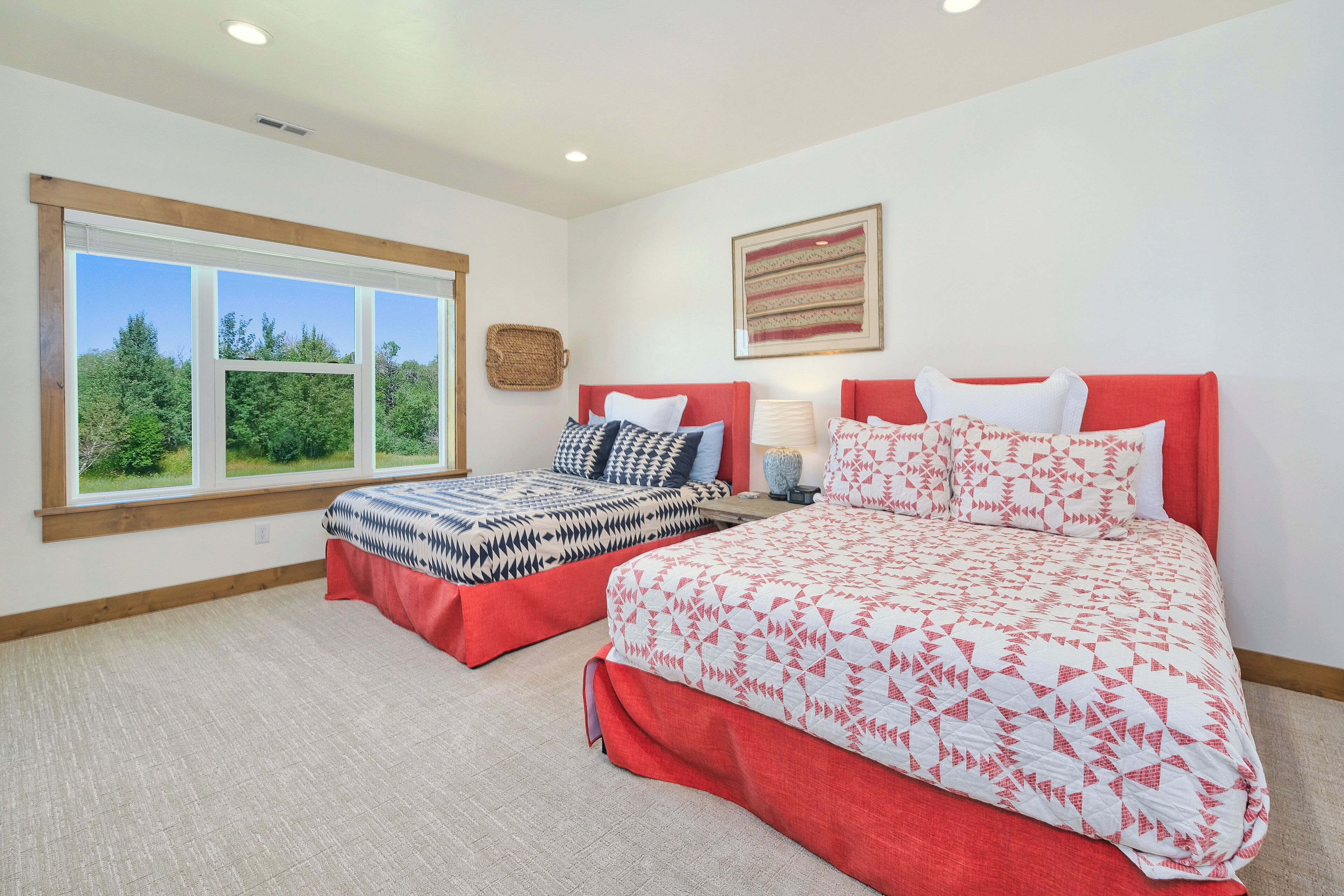 A bedroom with two beds, a large window, and a view of greenery.