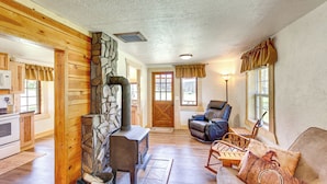 A cozy cabin interior with a stone fireplace, wooden walls, a leather sofa, and a dining area with a table and chairs. - Remote Custer Cabin w/ Fire Pit & Near State Park! (Custer)