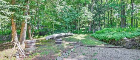 A forested area with a gravel path, a stone bridge, and a wooden barrel.