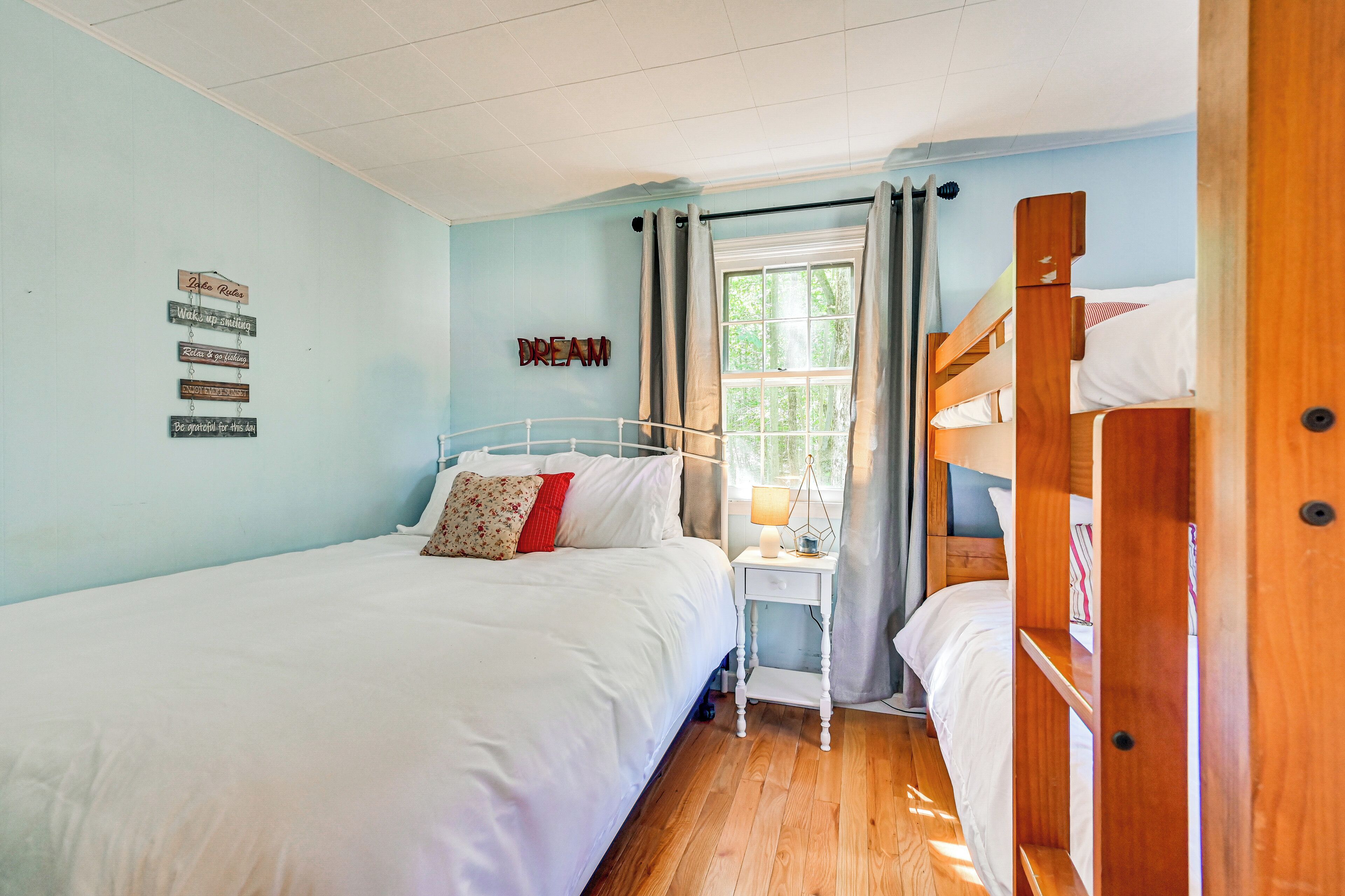 Een slaapkamer met een stapelbed, een enkel bed, een klein nachtkastje met een lamp en een raam met gordijnen.