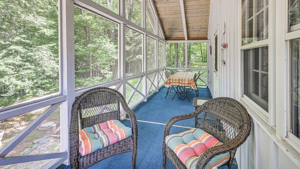 A covered porch with wicker chairs and a table, overlooking a forested area. - Becket Home w/ 3-season Porch: Walk to Lake Access (Becket)