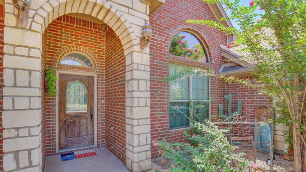 A brick house with a wooden front door, a small porch, and a garden with flowers and a metal chair. - Sunny Stephenville Home w/ Pool: 4 Mi to Downtown (Stephenville)