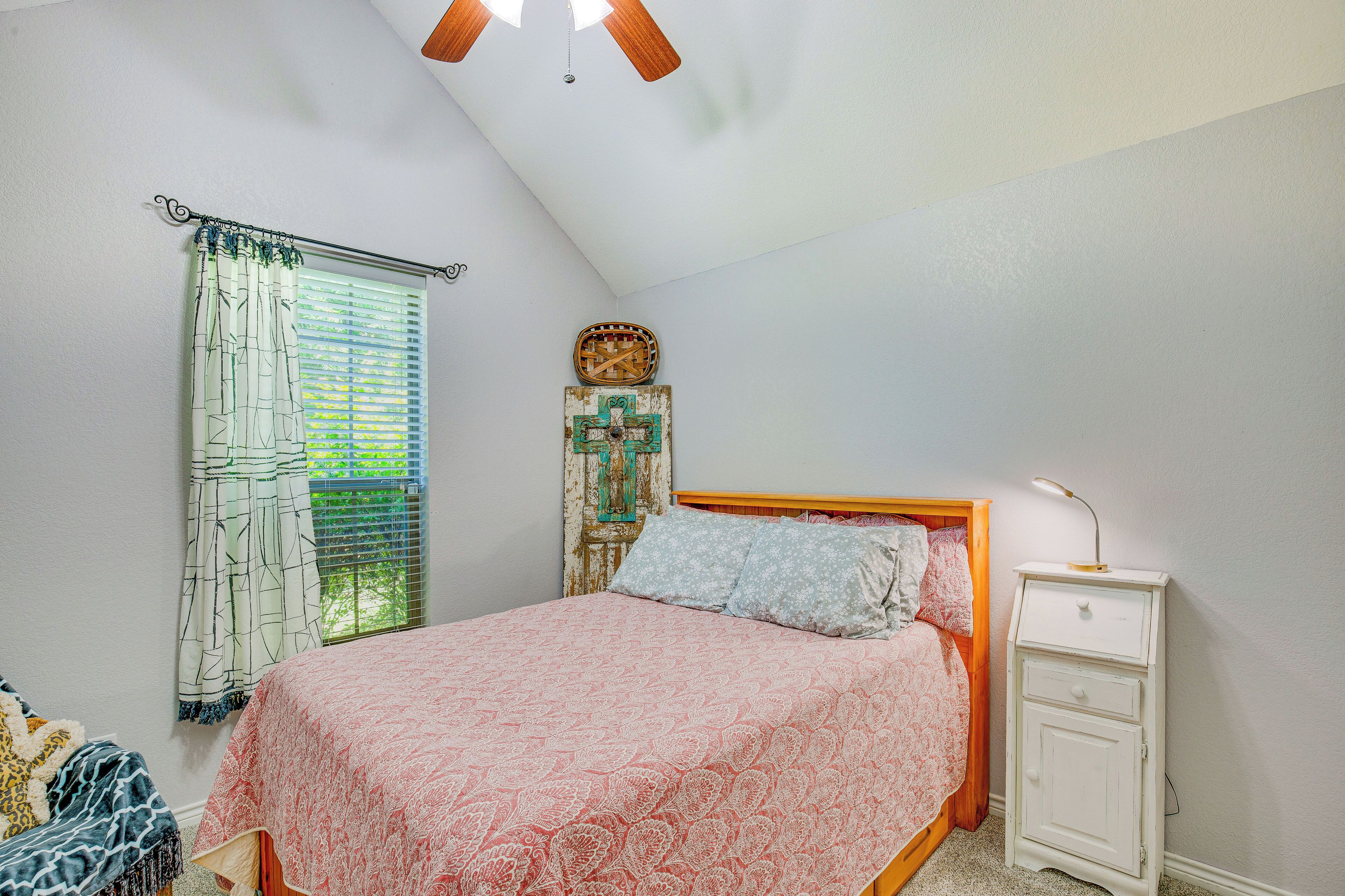 A bedroom with a bed, a nightstand, a ceiling fan, and a window with curtains.