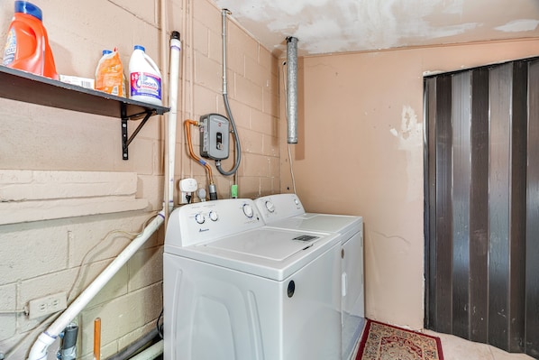 A laundry room with a white washer and dryer, a shelf with cleaning supplies, and a vent on the wall.