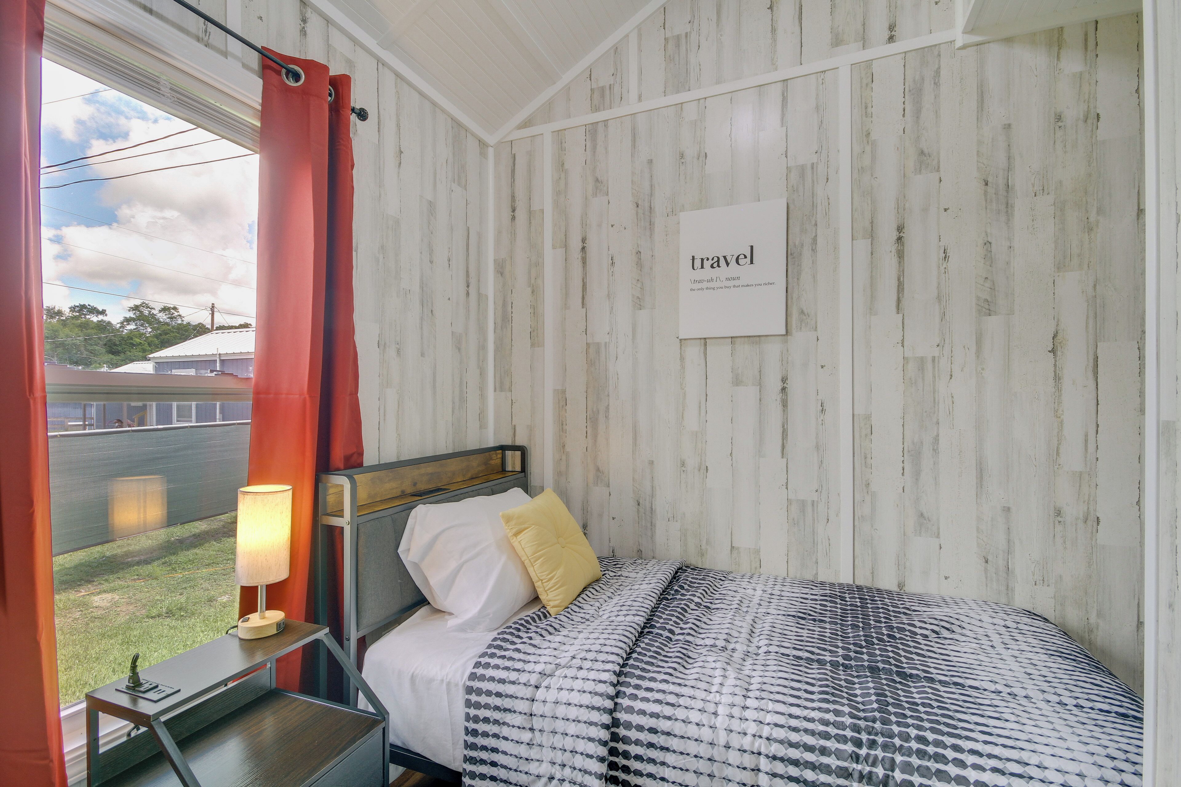 Een slaapkamer met een bed, nachtkastje, lamp en een raam met gordijnen.
