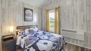 Un dormitorio con cama, mesita de noche, calefactor en la pared y ventana con cortinas.