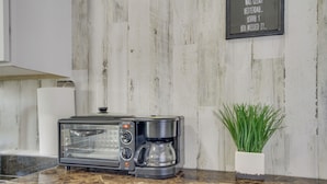 Una cocina con horno tostador empotrado, cafetera y planta en maceta sobre la encimera.
