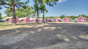 A row of pink cabins with a gravel driveway and pine trees in the foreground. - Picayune Tiny Home Rental ~ 11 Mi to Space Center! (Picayune)