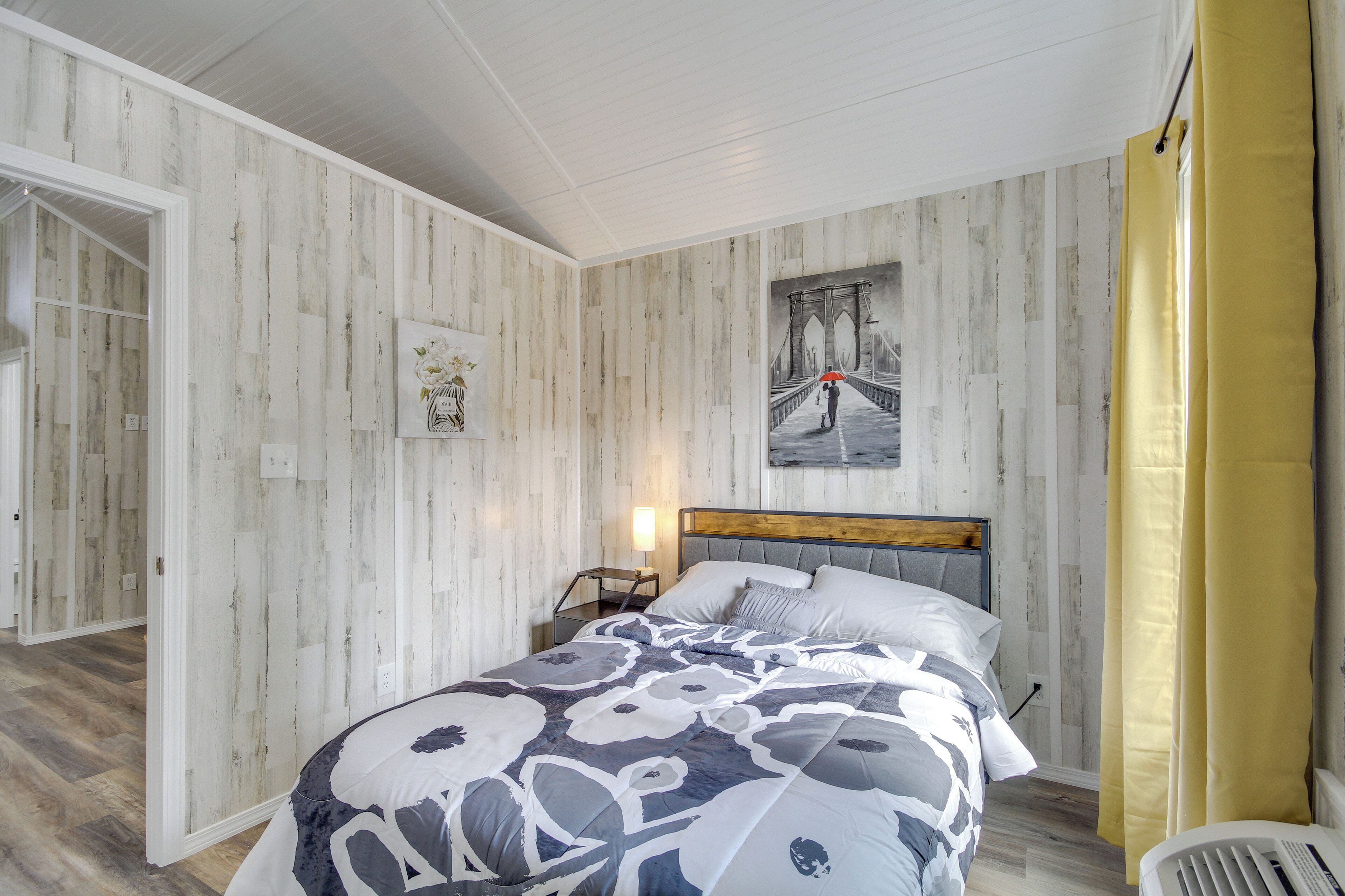 A bedroom with a bed, a nightstand, a wall-mounted lamp, and a painting of a bridge.