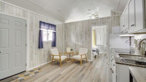 A modern kitchen with white cabinets, a granite countertop, and a built-in oven. There is a dining area with two white chairs and a small table. - Picayune Tiny Home Rental ~ 11 Mi to Space Center! (Picayune)