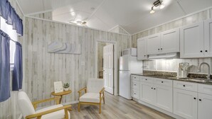 A kitchen with white cabinets, a microwave, and a refrigerator. There is a wooden chair and a small table with a plant. - Cozy Picayune Rental Home ~ 11 Mi to Space Center! (Picayune)