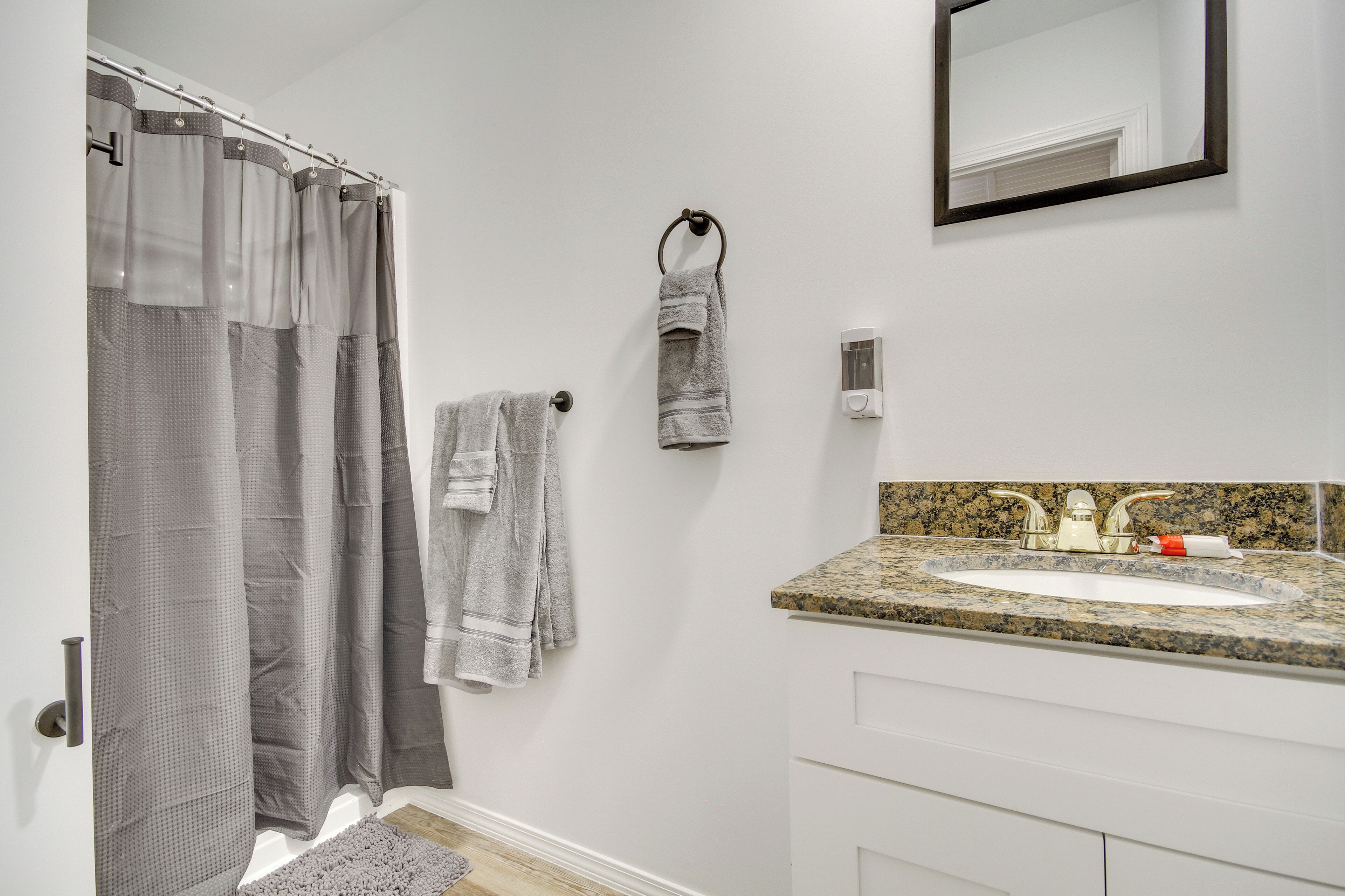 Une salle de bain avec un rideau de douche, un porte-serviettes avec des serviettes, un lavabo avec un plan de travail en granit et un miroir.