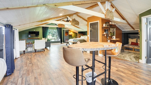 Un loft spacieux avec de hauts plafonds, des poutres apparentes, un coin cuisine et un espace repas agrémenté de tabourets de bar.