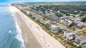 Vista aérea de una zona residencial costera con propiedades frente a la playa, una playa de arena y un cielo azul despejado.