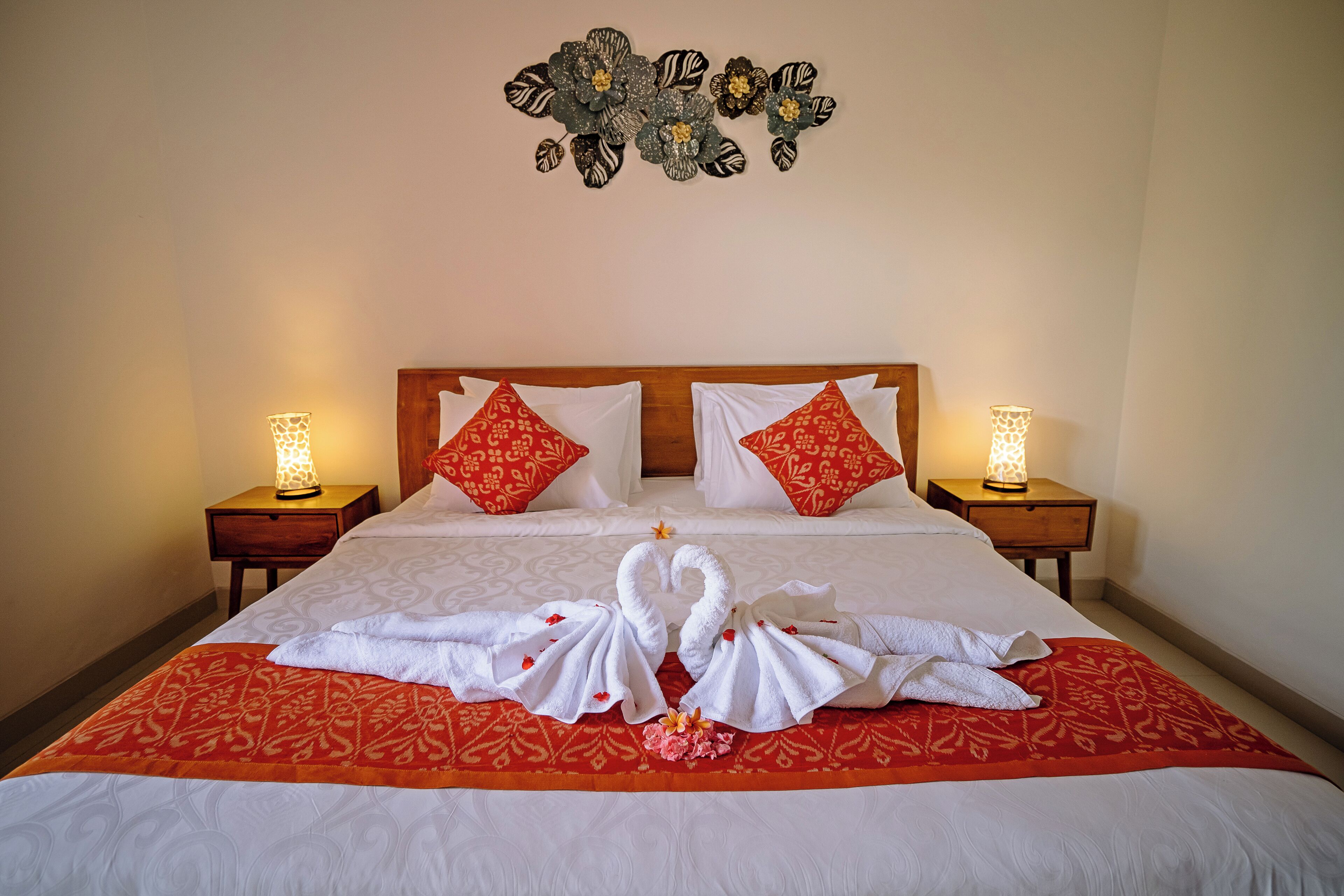 A neatly made bed with a red and white patterned bedspread, two pillows with red and white patterns, and a wall decoration above the bed.