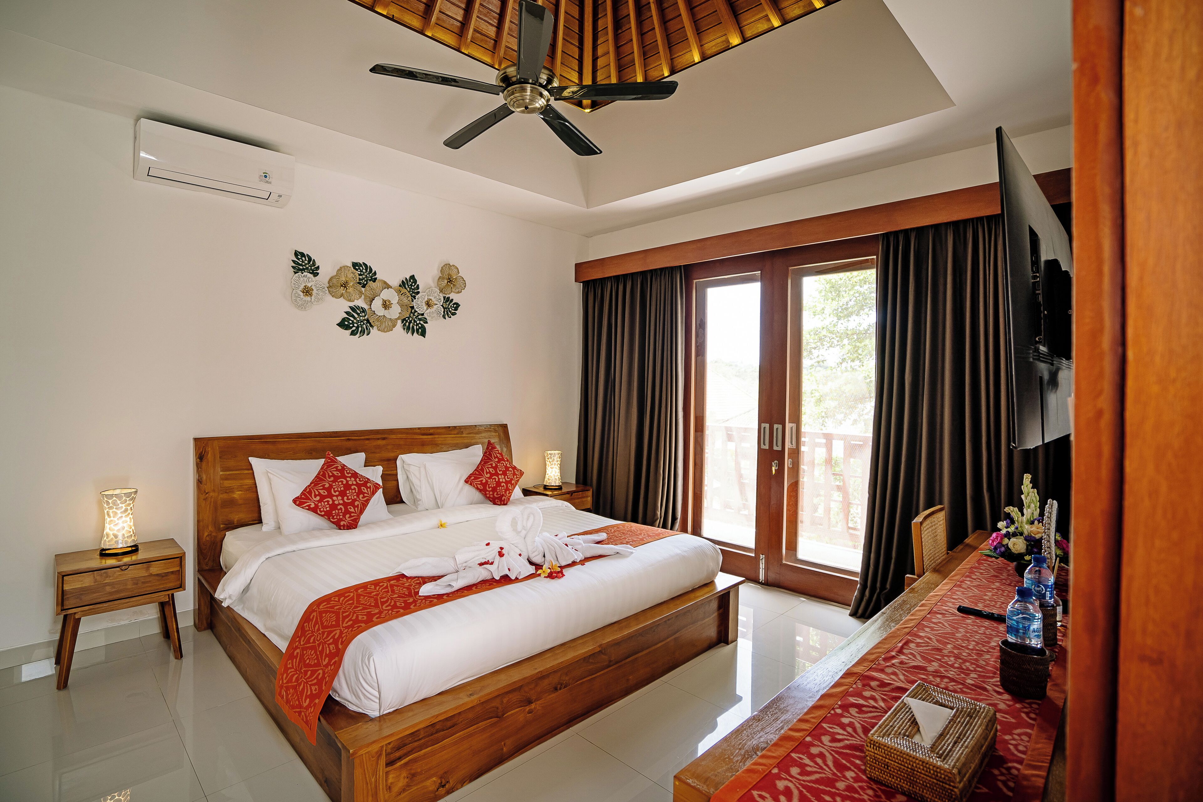 A spacious bedroom with a large bed, a ceiling fan, a TV, and a window with curtains.
