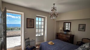 A bedroom with a large bed, a chair, a dresser, and a chandelier. There are two windows and a door leading to an outdoor area. - From the top of its terraces and garden, breathtaking views of the Luberon  (Murs)