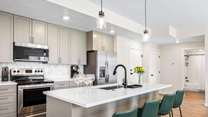 A modern kitchen with stainless steel appliances, a large island with bar stools, and pendant lighting. - Lagoon Desert Retreat (St. George)