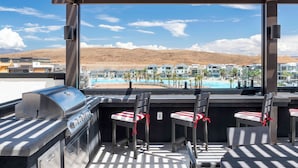 A rooftop bar with a grill, chairs, and a view of a pool and buildings. - Lagoon Desert Retreat (St. George)