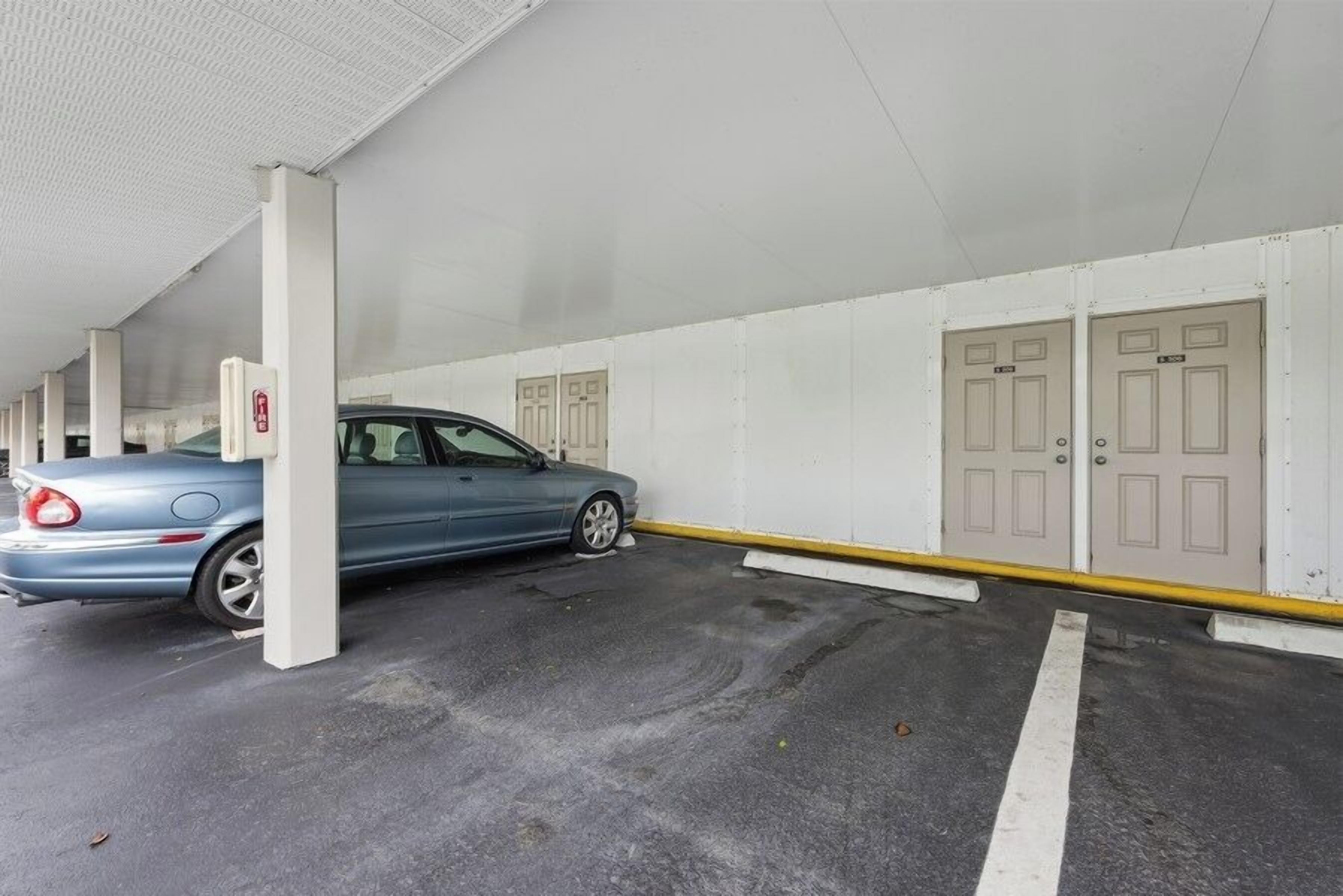 Eine Tiefgarage mit einem blauen Auto, das in der Nähe einer Säule geparkt ist, weißen Wänden und Türen mit Nummern.