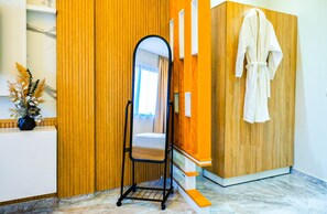 Ein Badezimmer mit einem Holzbadezimmermöbel, einem Spiegel, einem an der Wand hängenden Bademantel und einer kleinen Pflanze auf der Ablagefläche.