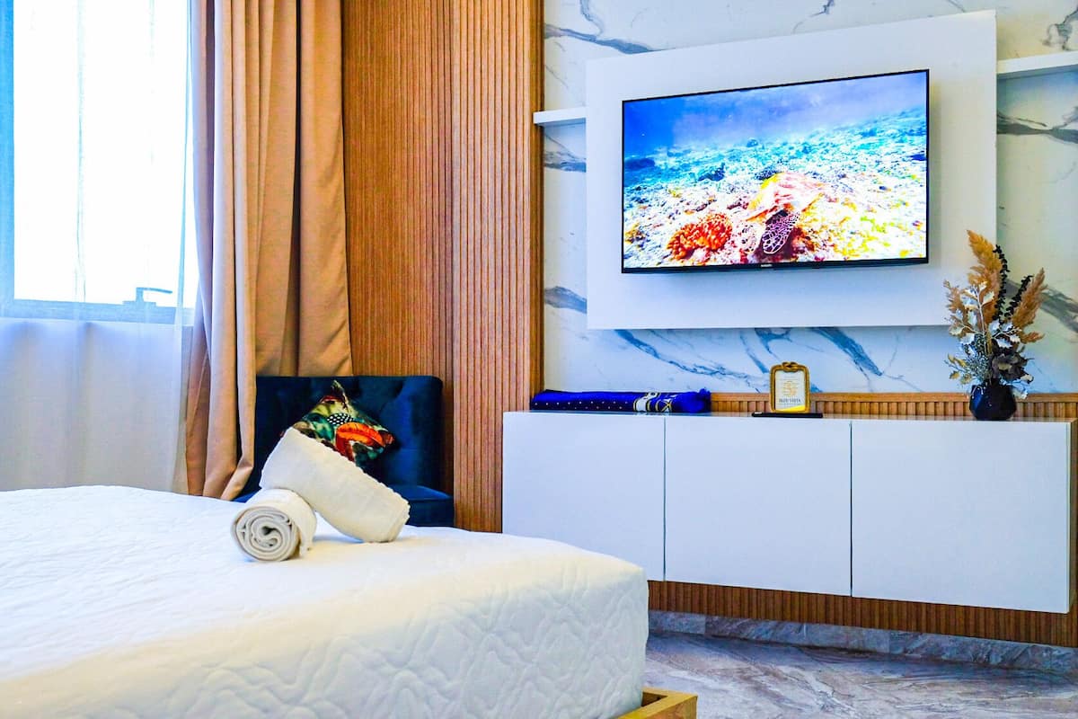 Una habitación de hotel con una cama, un televisor en la pared, una silla azul y un mueble de madera.