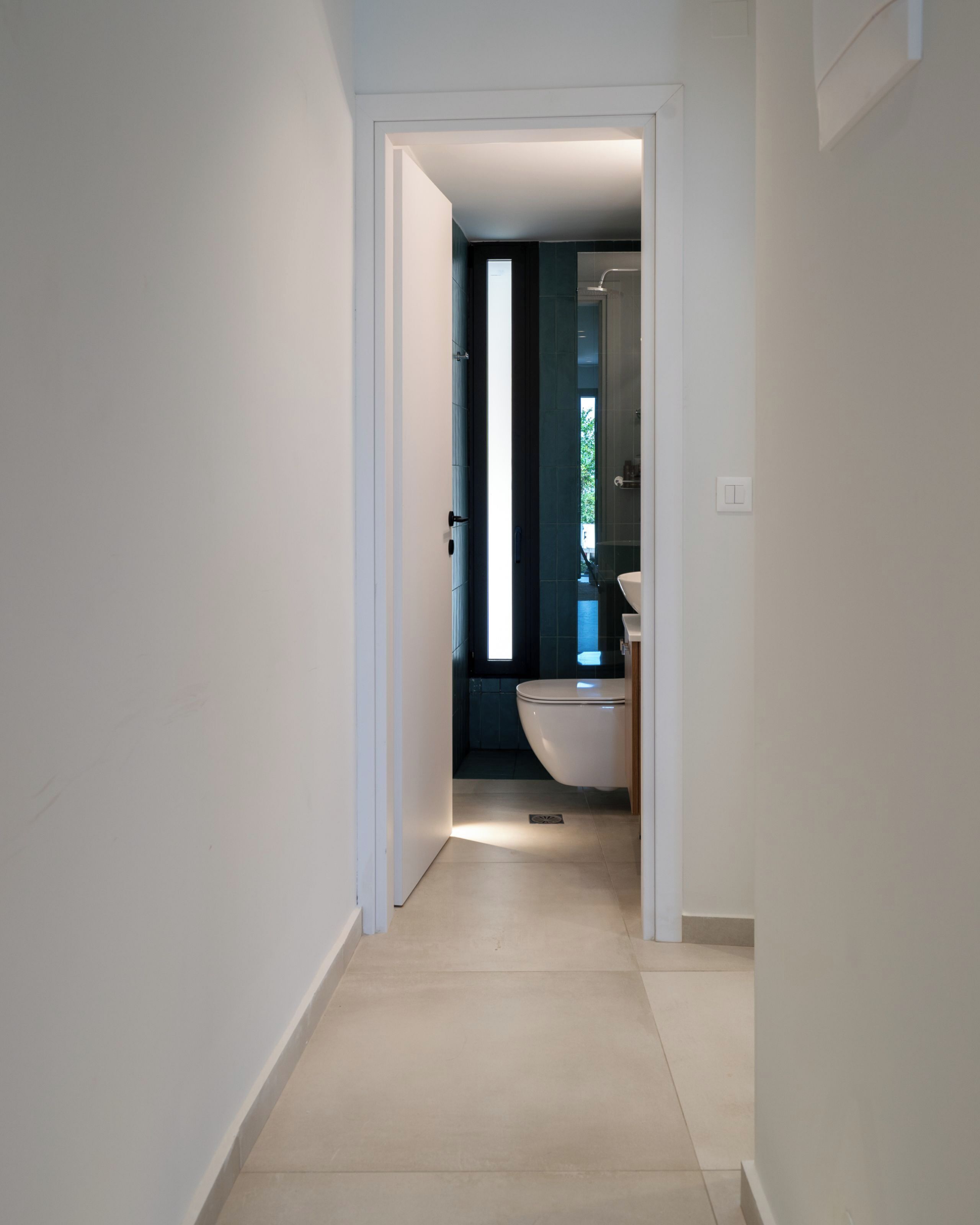 Een smalle gang die leidt naar een badkamer met toilet en wastafel.