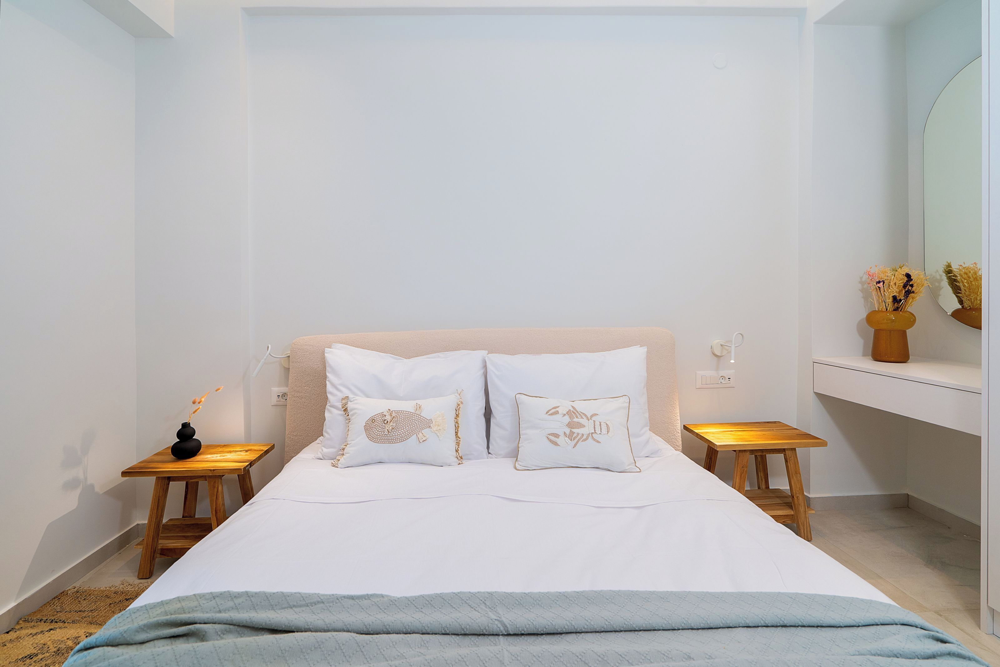 Une chambre à coucher comprenant un lit, deux tables de chevet, une commode, un miroir et une petite étagère ornée d’objets décoratifs.