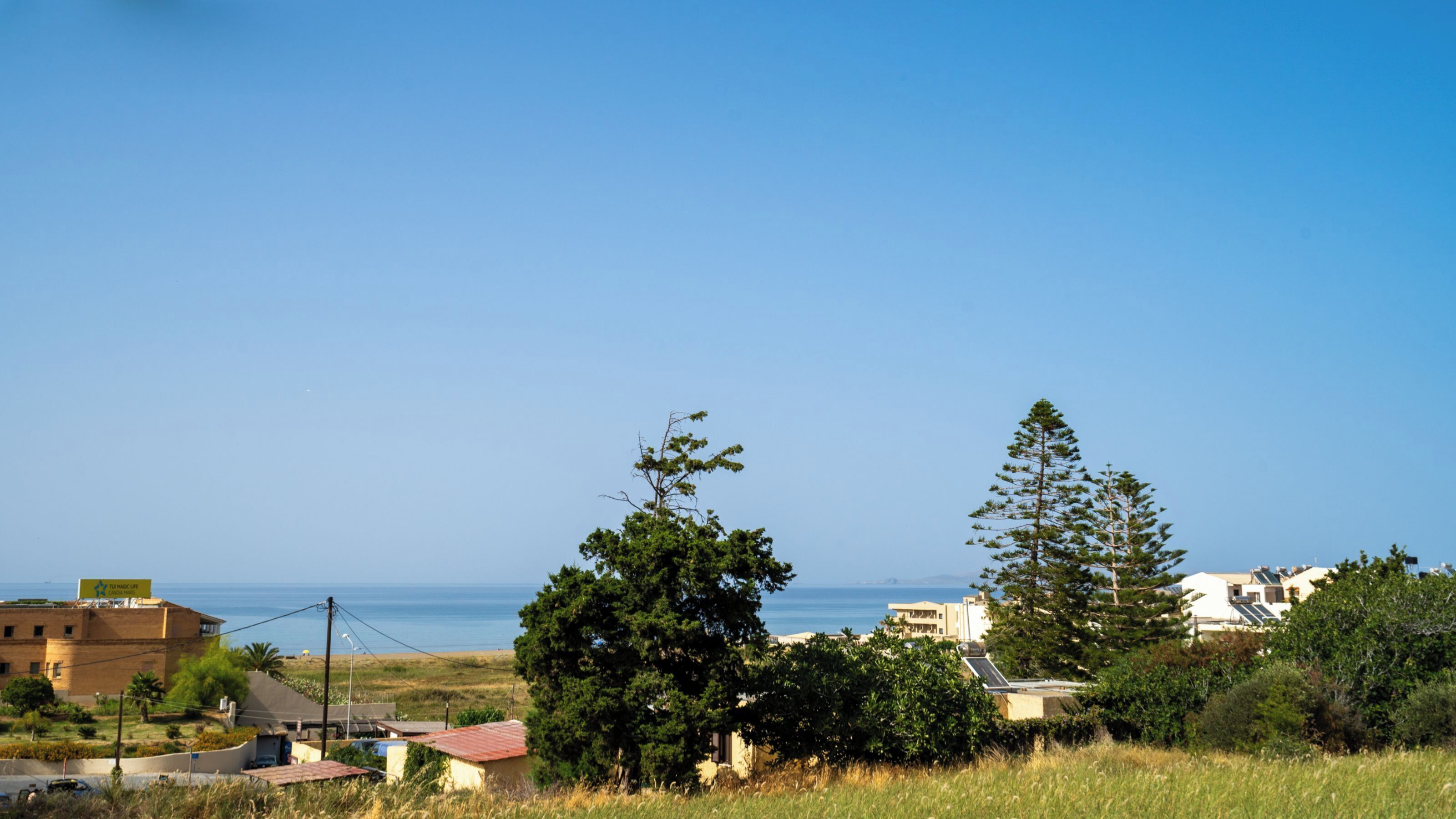A coastal residential area with houses, trees, and a clear view of the sea.