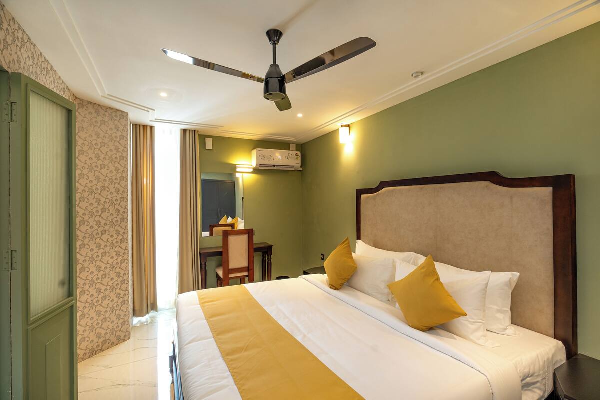 A hotel room with a bed, a ceiling fan, an air conditioning unit, and a desk with a chair.