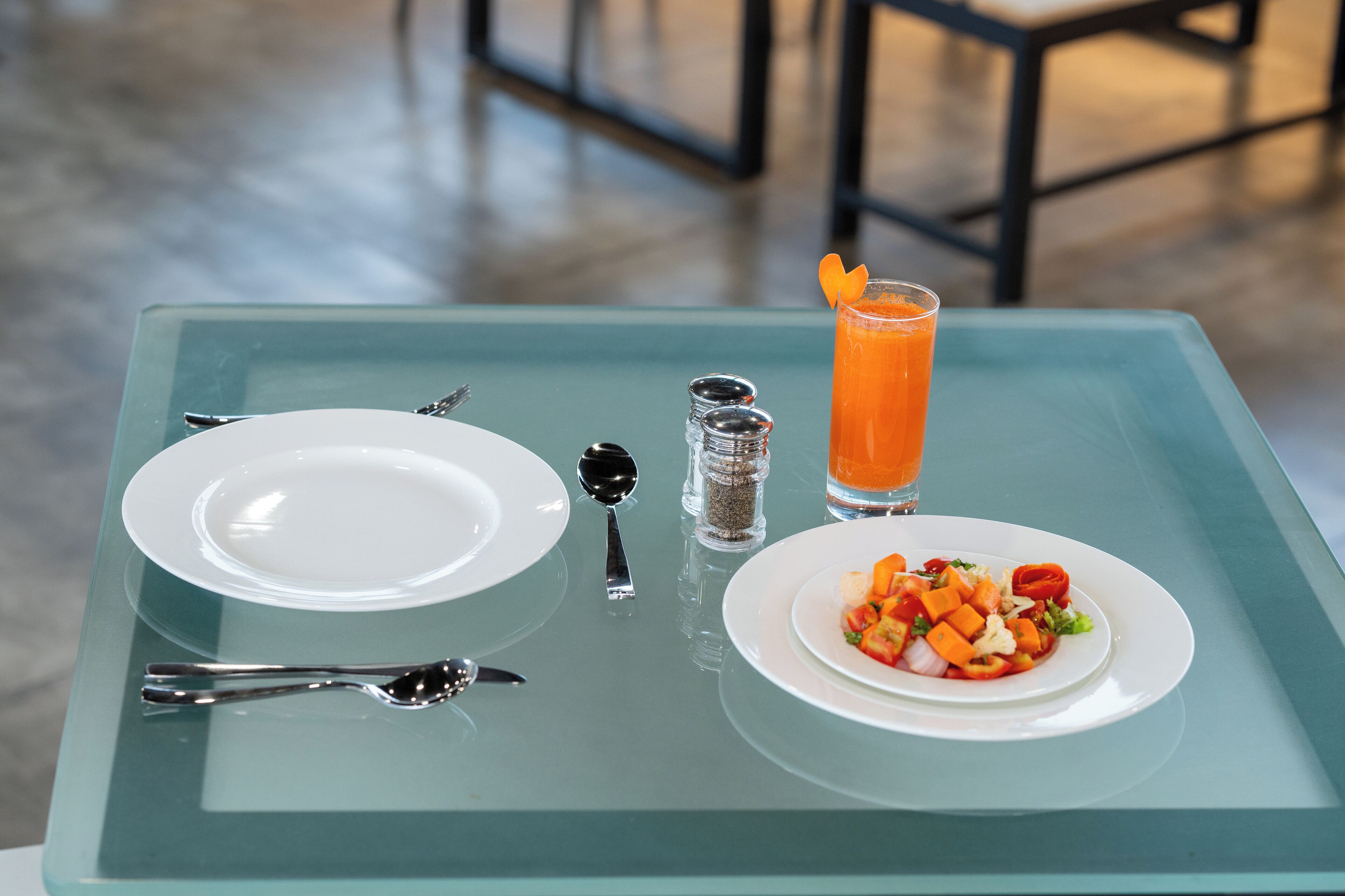 A table with a glass tray, two white plates, a glass of orange juice, and a plate of mixed vegetables.