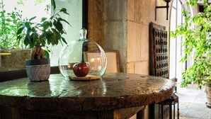 Una mesa redonda de madera con una lámpara de cristal en el centro, una planta en maceta y una manzana roja.