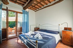 Un dormitorio con una cama, una mesita de noche de madera, un aparador y un ventanal corredera que da a un patio exterior.