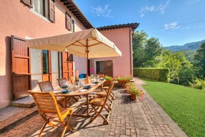 Un patio con una mesa lista para comer, un paraguas cubierto y vistas a un paisaje verde.