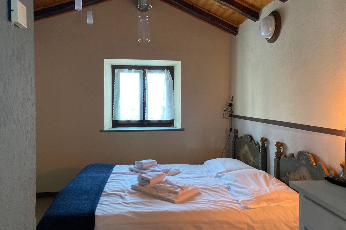 A bedroom with a bed, a window, a nightstand, and a wall-mounted light fixture.