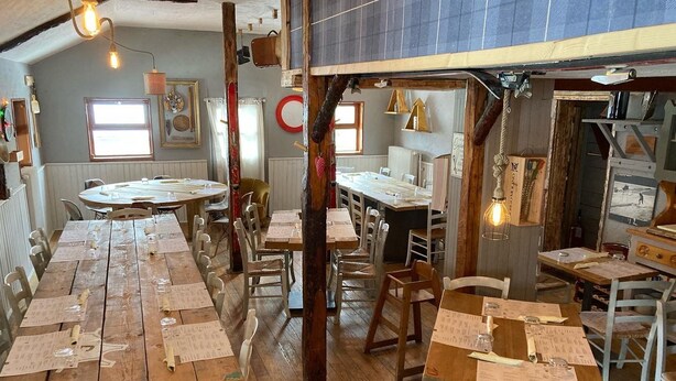 Un comedor rústico con mesas y sillas de madera, vigas a la vista y lámparas colgantes.