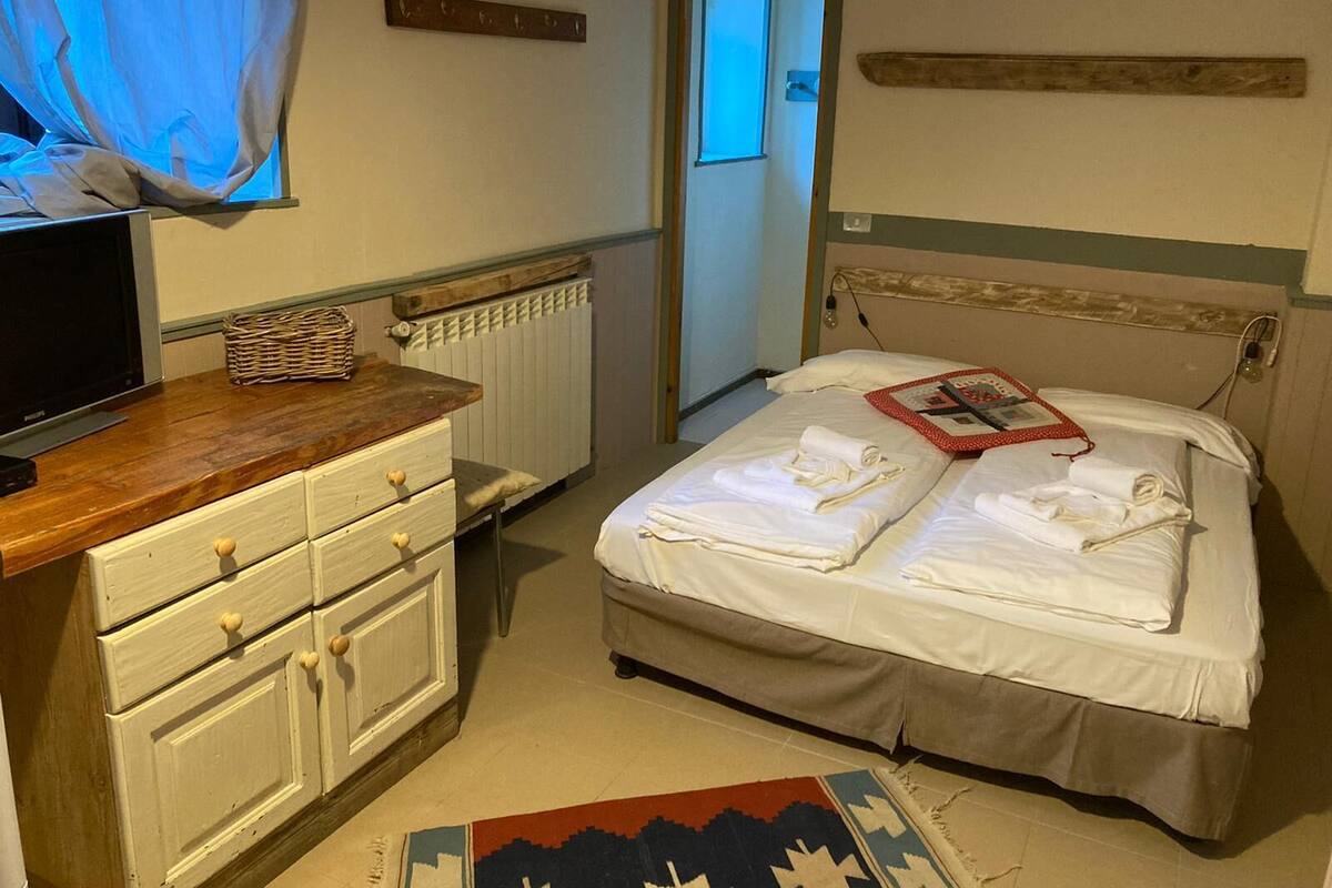 A bedroom with a bed, a wooden dresser, a television, and a window with curtains.