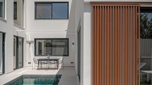 Una casa moderna amb una piscina, zona de menjador i un gran finestral corredís.