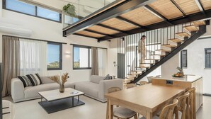 Àmplia zona d'estar amb una escala moderna, una taula de dinar i un sofà.