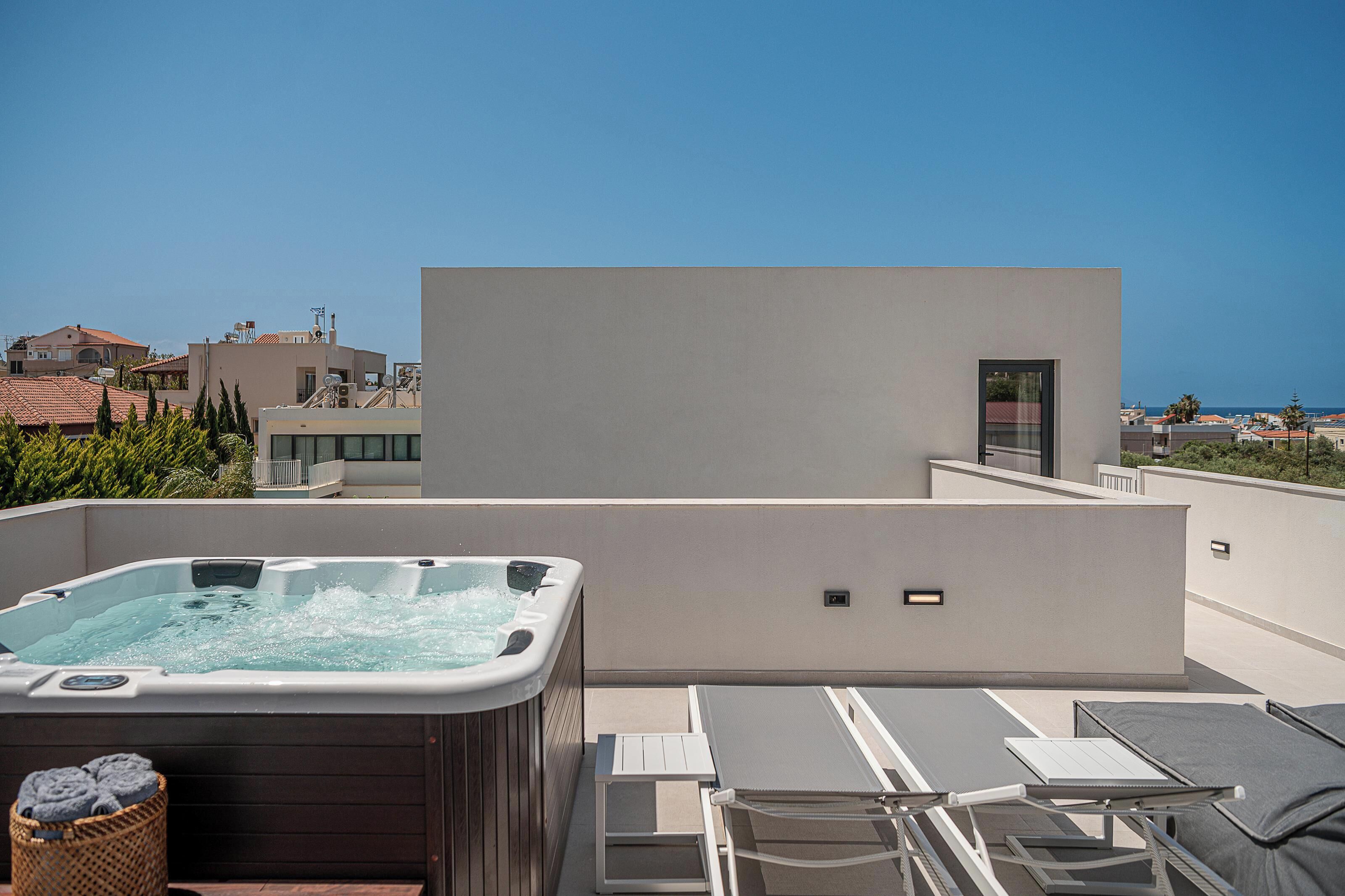 A rooftop terrace with a hot tub, lounge chairs, and a view of the sea.