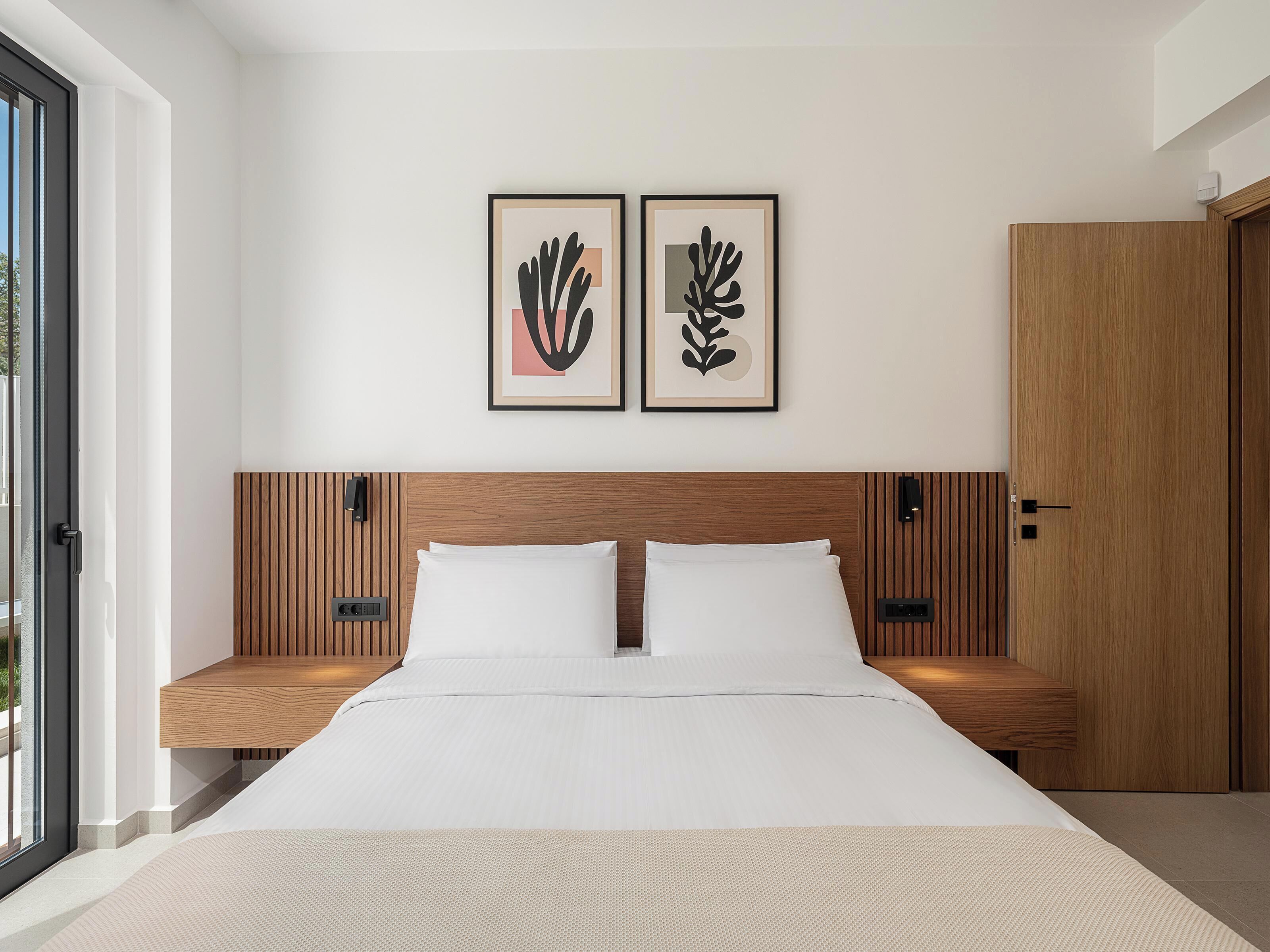 A modern bedroom with a large bed, wooden paneling on the walls, two framed abstract artworks, and a wooden wardrobe.