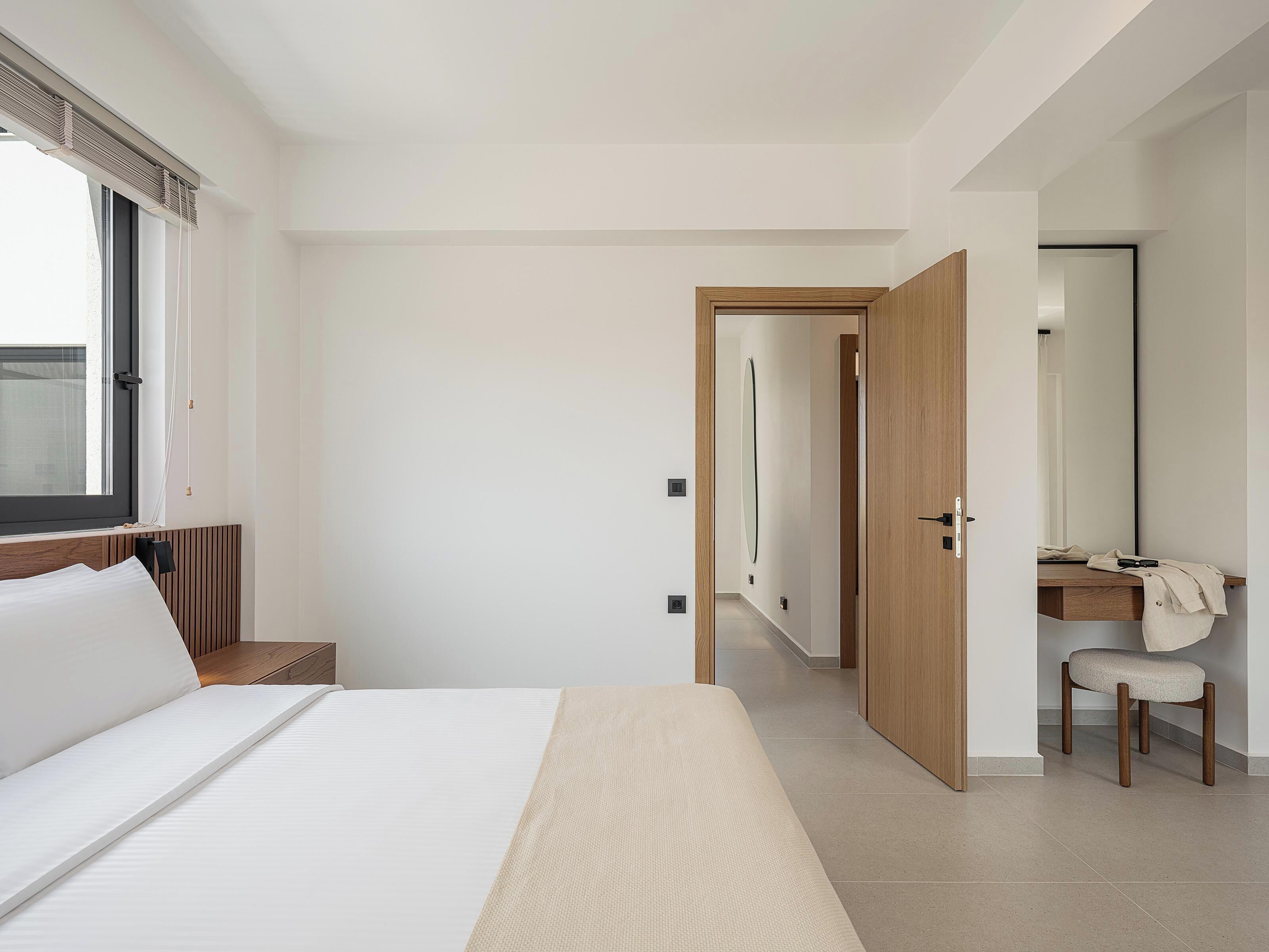 Une chambre d’hôtel moderne avec un grand lit, une table de chevet en bois, une lampe de chevet, un miroir et une chaise.