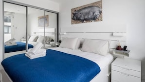 Une chambre d’hôtel avec un grand lit, une table de chevet, une commode, un miroir et une œuvre d’art représentant un cochon, accrochée au mur.